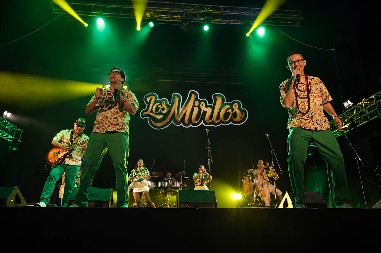 Los Mirlos en vivo sobre escenario con iluminación verde y letrero luminoso de la agrupación.