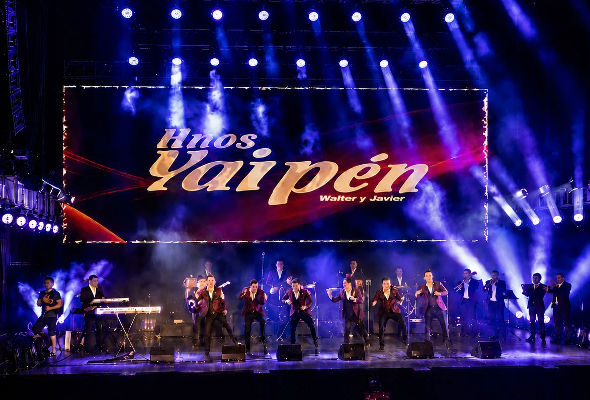 Hnos. Yaipén sobre escenario con pantalla LED, humo e iluminación azul en concierto.